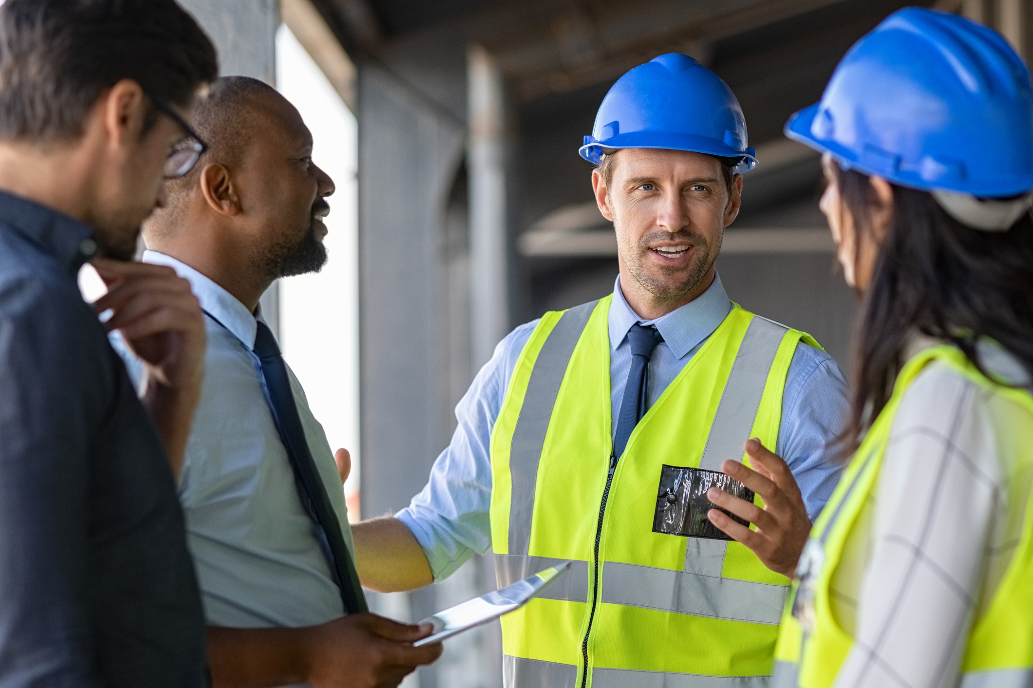 Happy mature engineer discussing the structure of the building with architects colleague at construction site. Engineers wearing safety hardhat having work conversation on the safety of the structure. Multiethnic team of business men and workers talking at site.